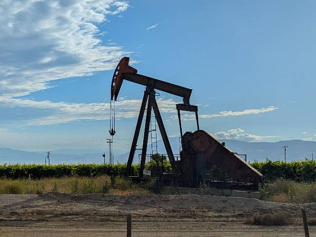 oil well pump jack against bright blue sky and distant mountains