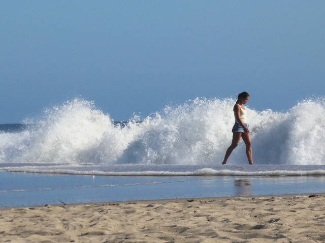 photo of large crashing waves with a woman walking in foreground