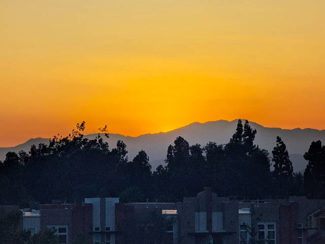 sunset over rolling hills with trees and dwellings below