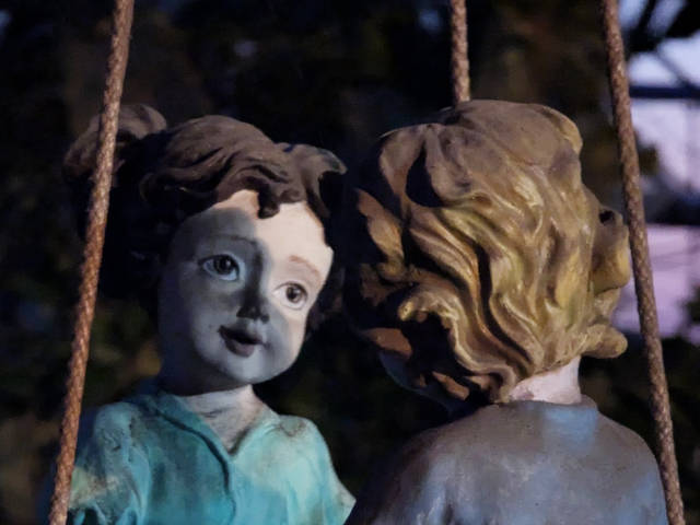 creepy, weathered statuette of boy and girl on a tire swing smiling at each other